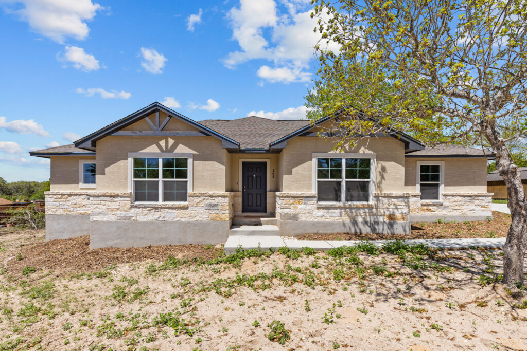 Exterior view of a newly constructed home in Alanna Heights with a stone and stucco facade. The home features a dark front door, multiple windows, and a sloped roof.